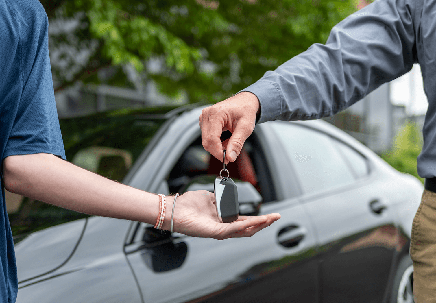 Parent handing over keys to their teen in front of a car